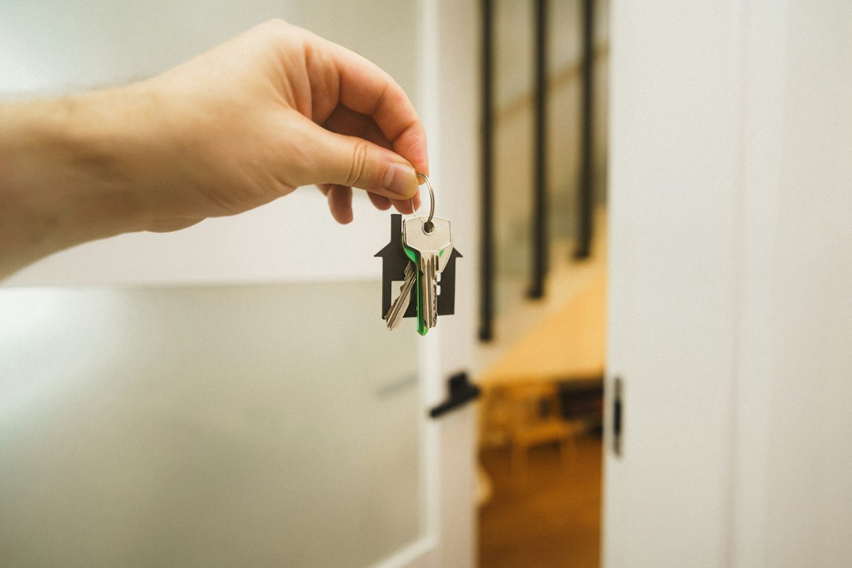 Main tenant les clés d’une maison devant la porte d’entrée, accueil d’un voyageur en location saisonnière