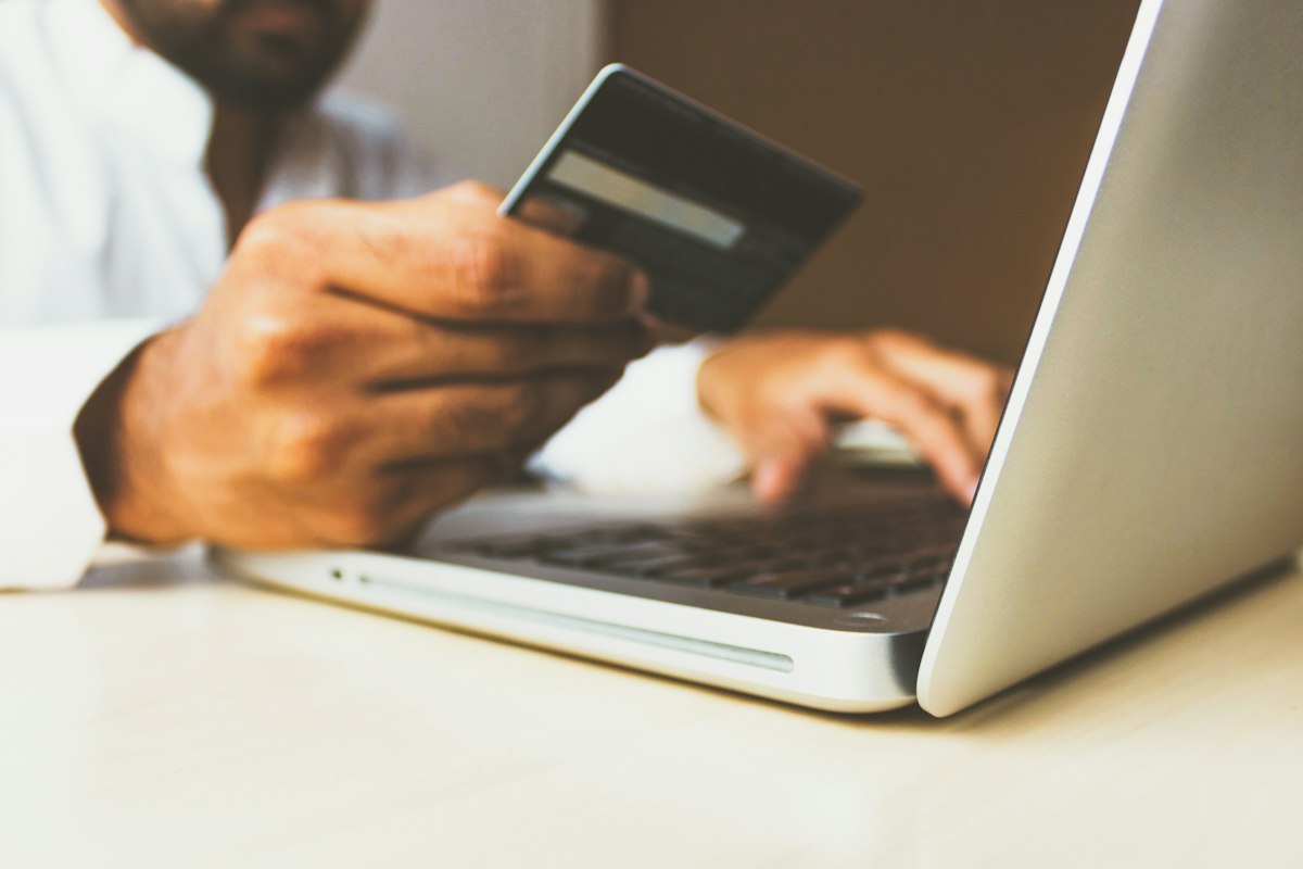 Voyageur qui tient sa carte bancaire devant un ordinateur portable pour réserver en ligne