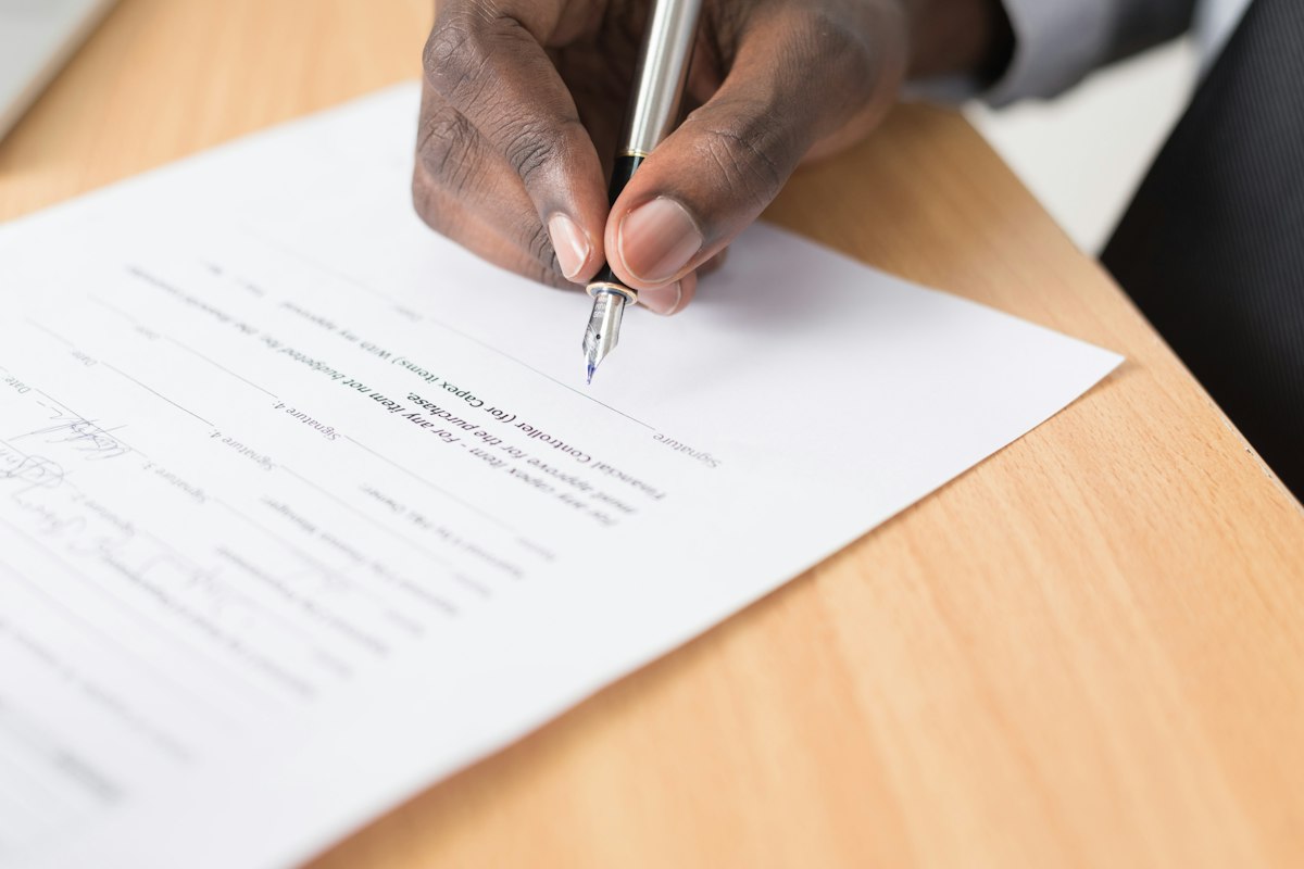 Main qui signe un contrat de location saisonnière sur une table en bois