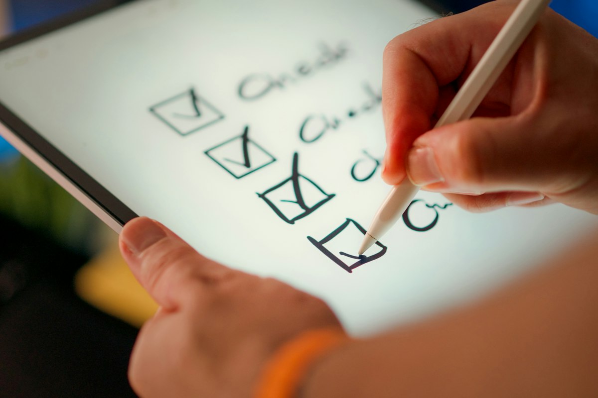 Main qui coche une liste de contrôle sur une tablette, comme pour un état des lieux numérique